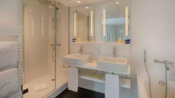 Un baño moderno con ducha envuelta en vidrio, dos lavamanos y una bañera.
