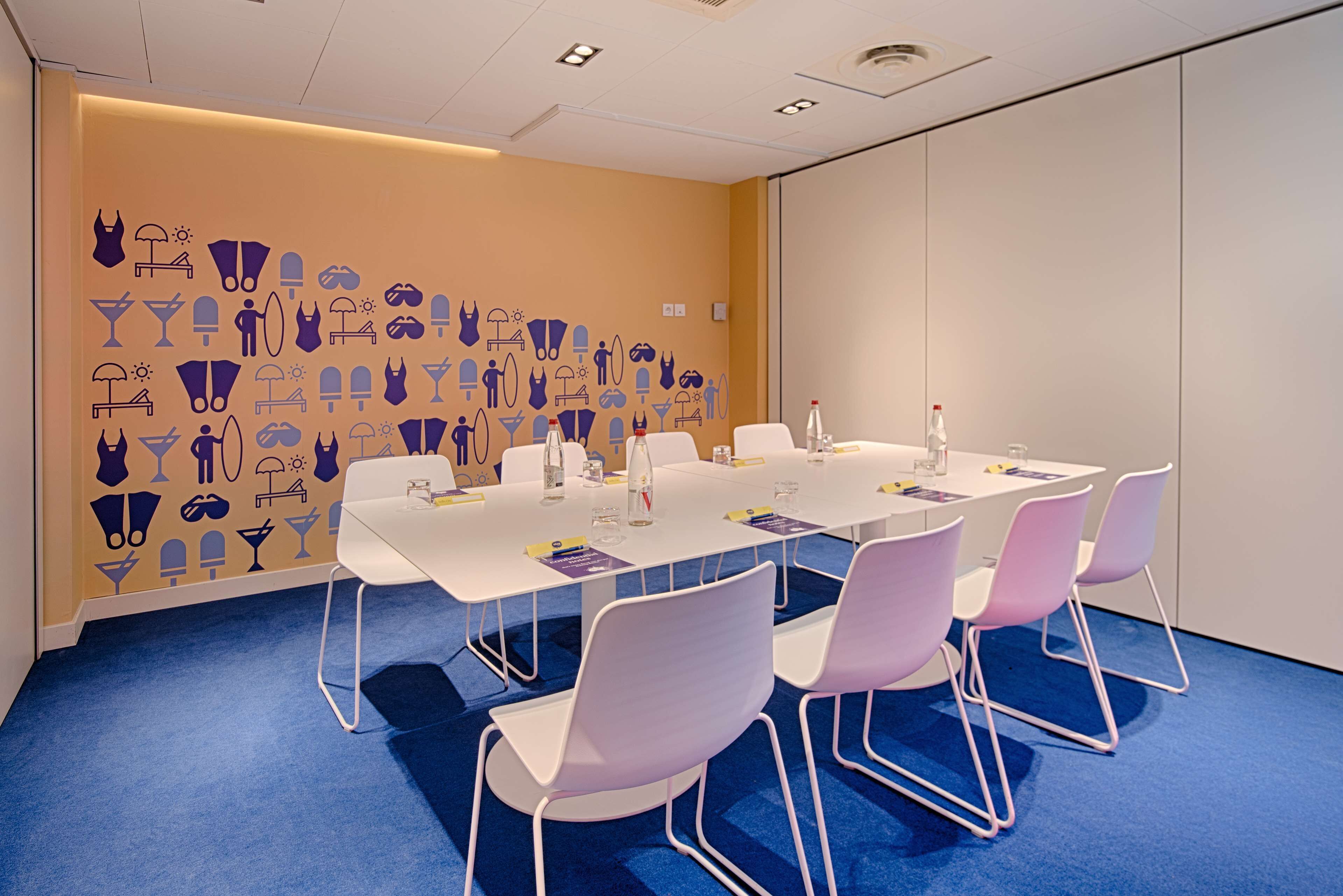 Une salle de conférence avec une longue table, des chaises blanches et un mur orné de différents pictogrammes.