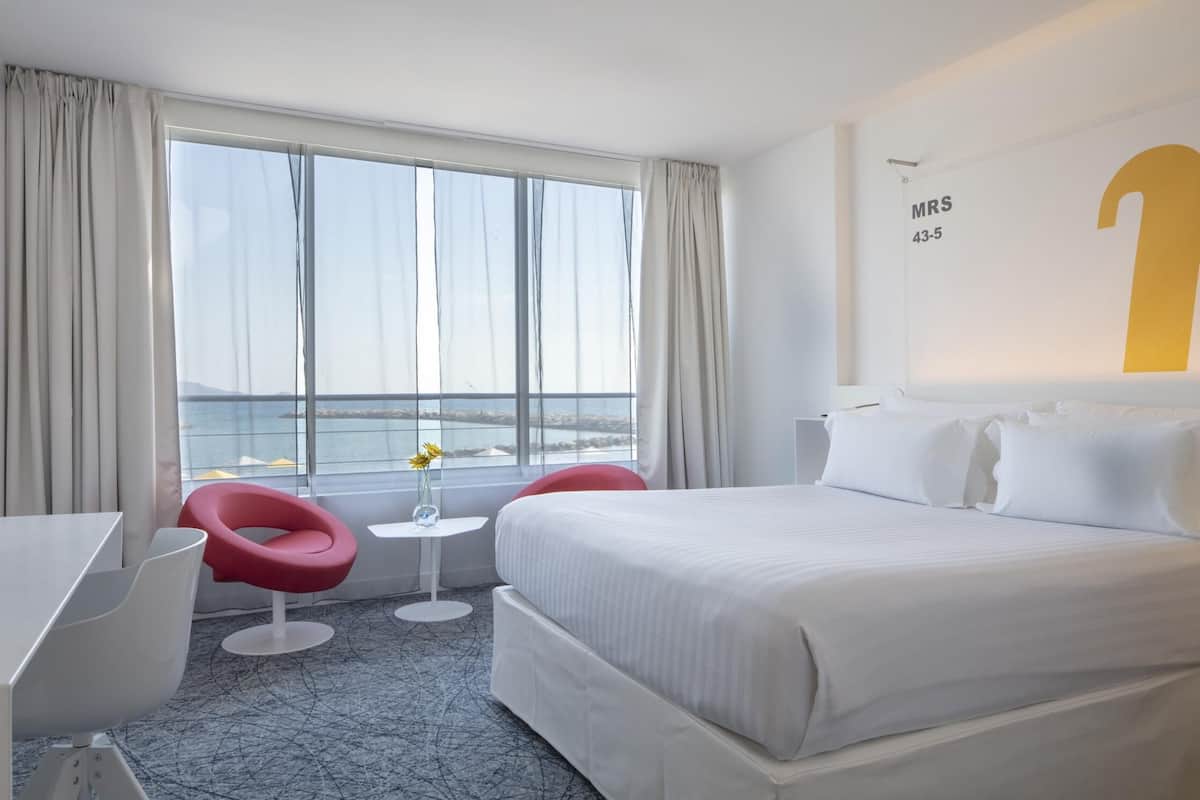 Habitación de hotel con una cama grande, un escritorio, una silla y vista al mar.