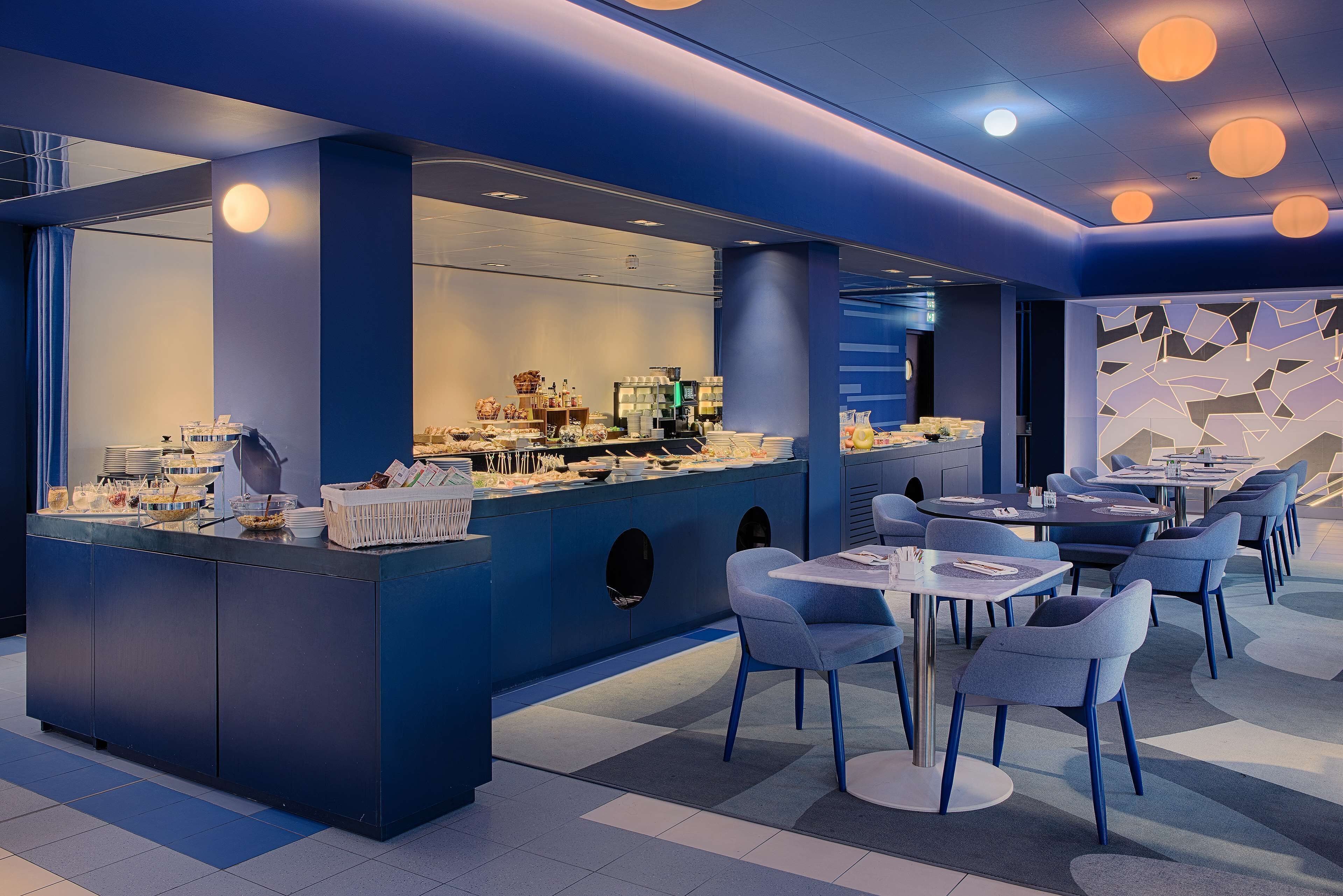 Ein modernes Restaurant mit blauem Farbkonzept, das eine Selbstbedienungsbar und einen Sitzbereich mit Tischen und Stühlen bietet.