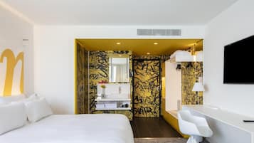 Una habitación de hotel moderna con una cama grande, un escritorio y un baño con espejo y lavamanos.