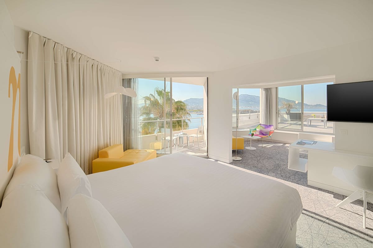 Una habitación de hotel con una cama grande, un balcón con vistas a la ciudad y un televisor de pantalla plana.