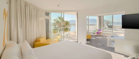 A hotel room with a large bed, a balcony with a view of the city, and a flat-screen TV.
