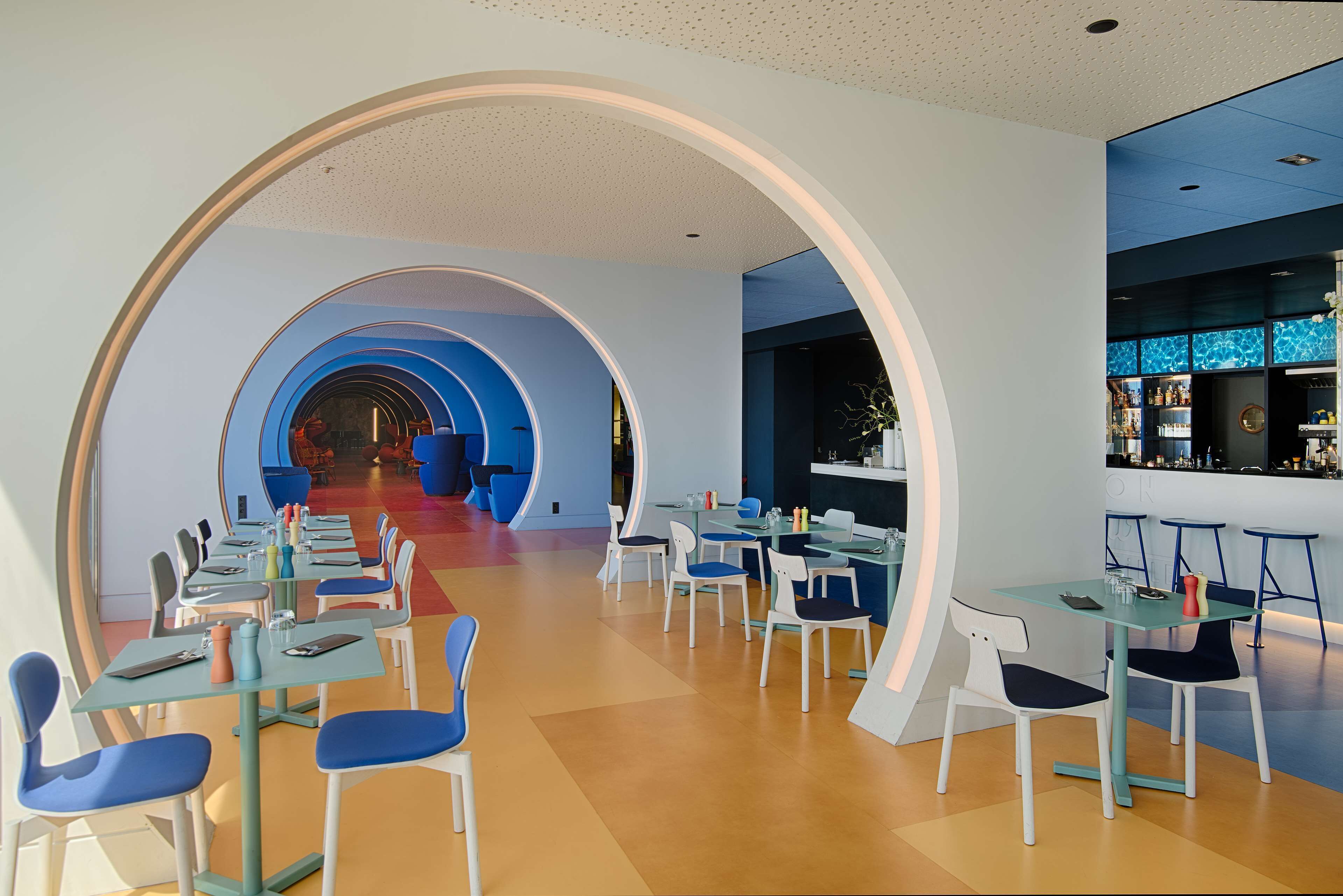 A modern restaurant with a long counter, blue chairs, and a bar area.