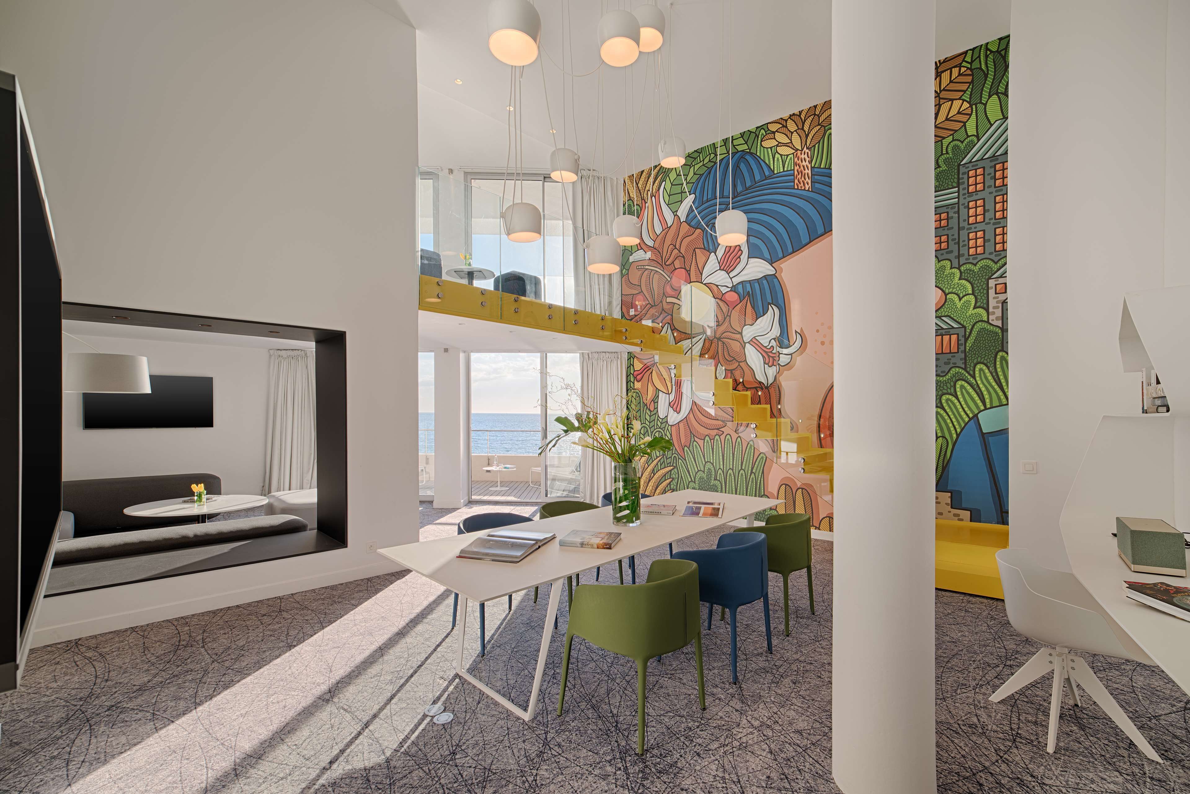 A modern interior with a dining area, colorful mural, and a view of the sea.