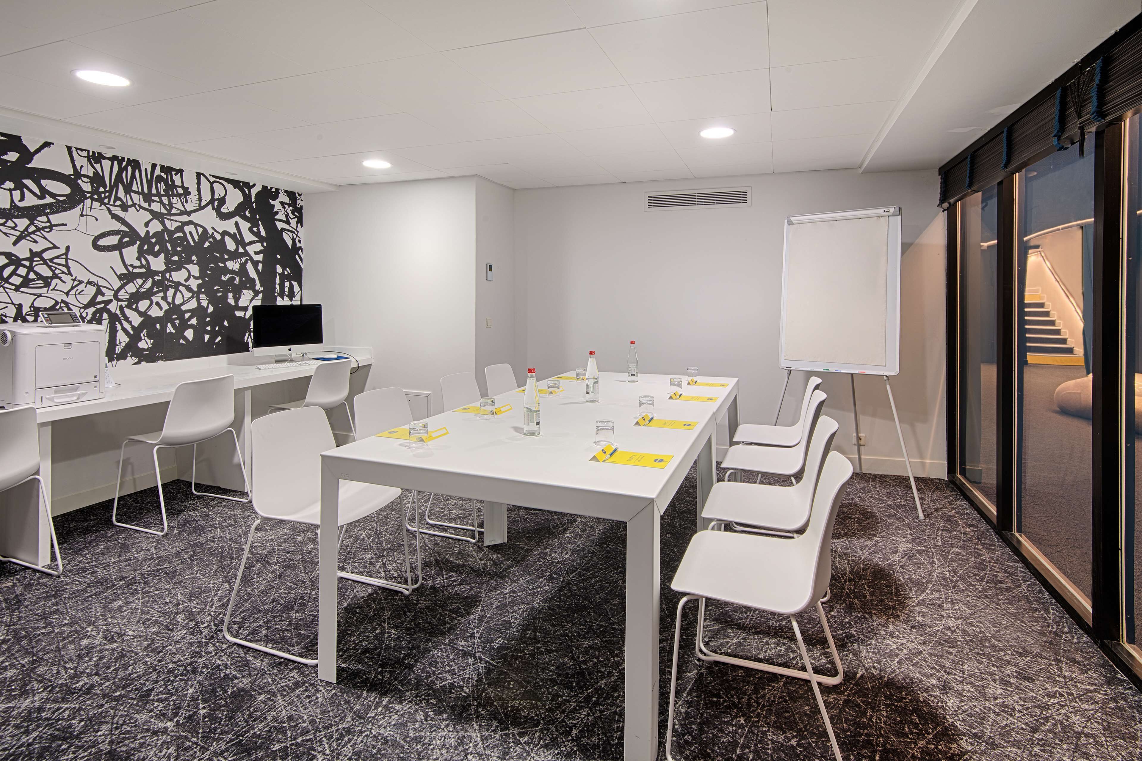 Ett konferensrum med ett långt bord, vita stolar, en whiteboard och en stor, abstrakt målning på väggen.
