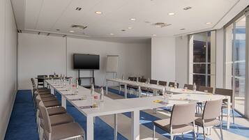 A conference room with long tables, chairs, a projector screen, and a whiteboard.