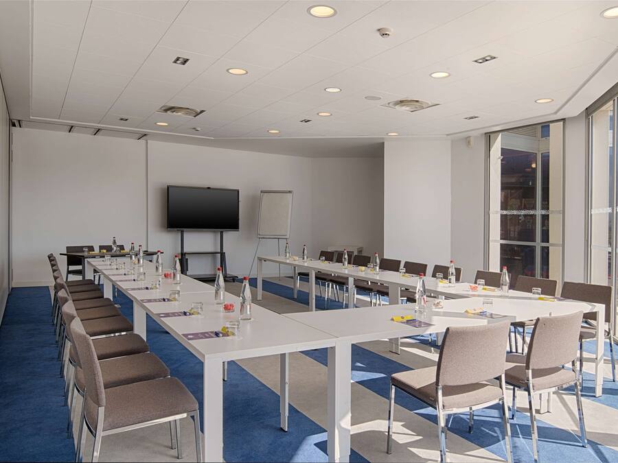A conference room with long tables, chairs, a projector screen, and a whiteboard.