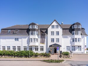 A white building with a black roof, multiple windows, and a flag. - PLAZA Premium Sylt (Wenningstedt-Braderup)