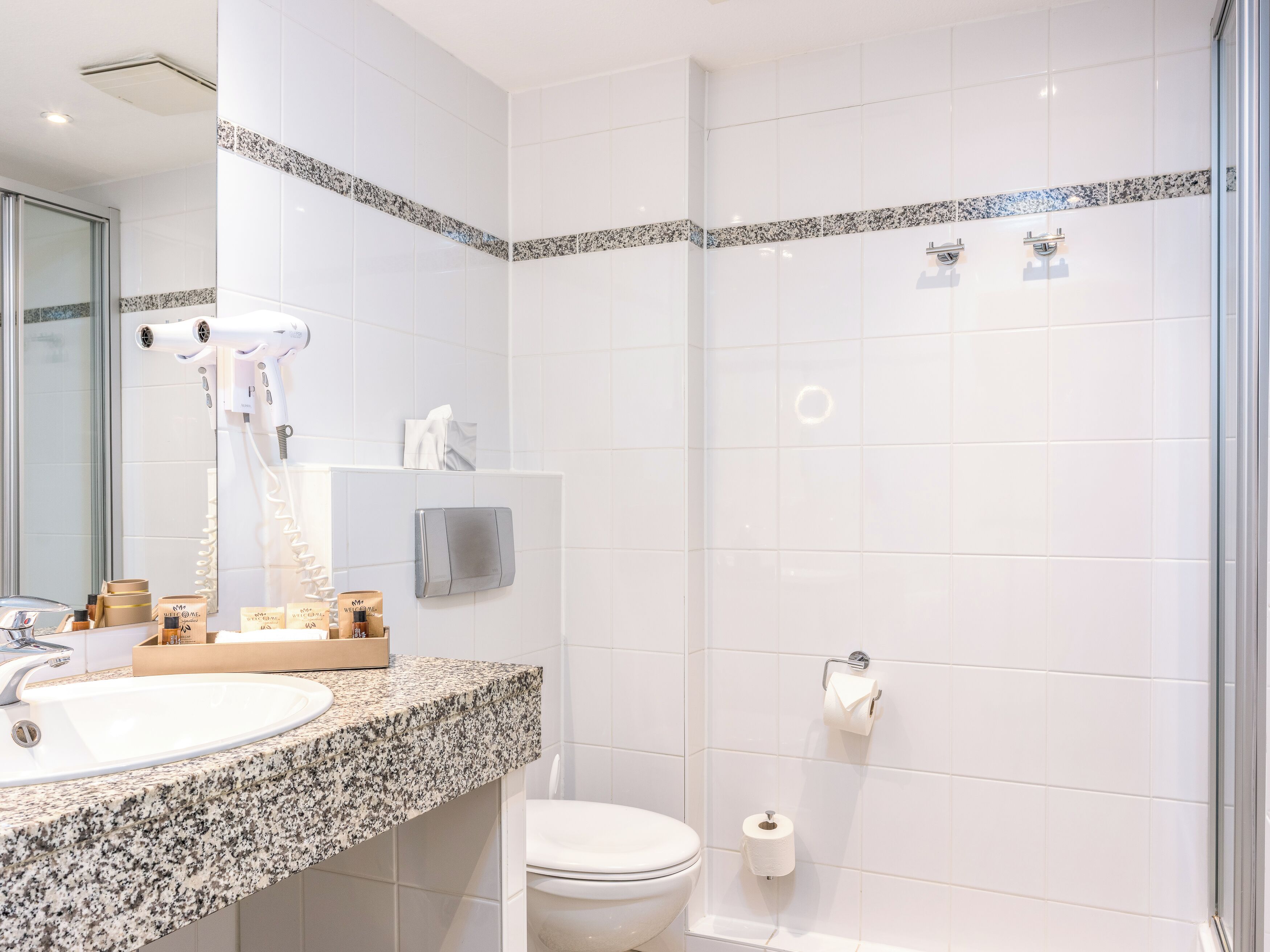 A modern bathroom with a granite countertop, a white sink, a hairdryer, and a toilet.