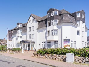A multi-story building with a white facade and dark roof, featuring a prominent entrance with a sign. - PLAZA Premium Sylt (Wenningstedt-Braderup)