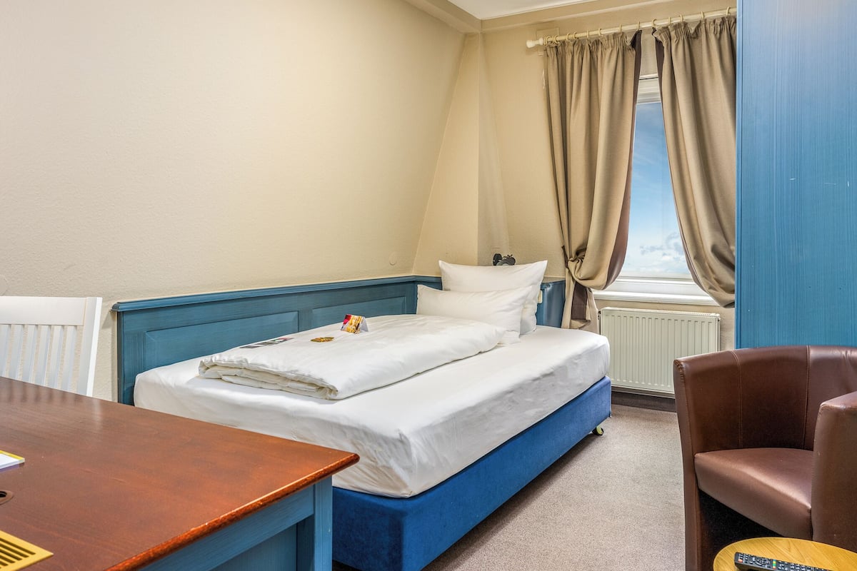 A room with a bed, a desk, a chair, and a window with curtains.