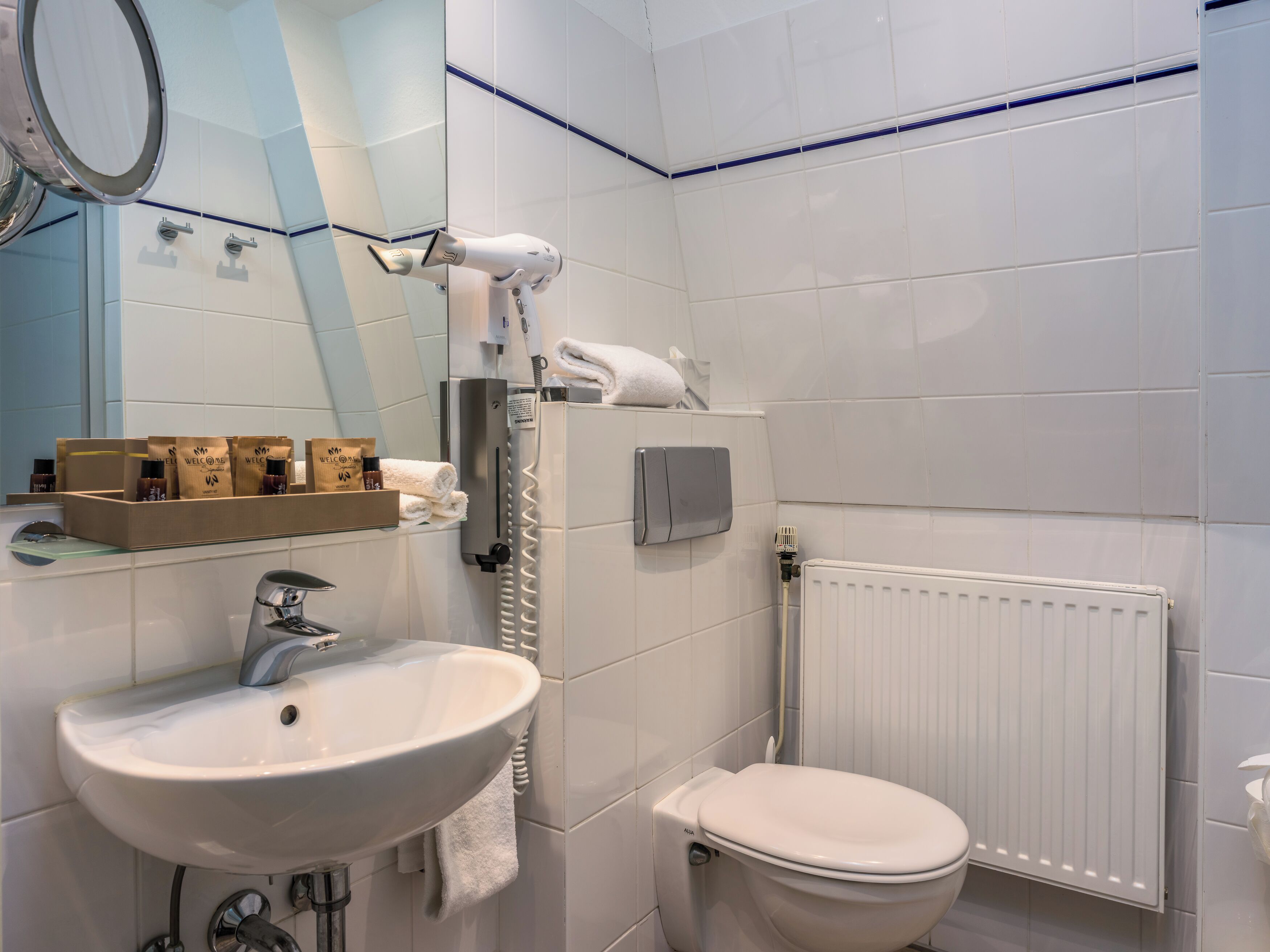 Een moderne badkamer met een wit wastafel, toilet en een haardroger aan de muur.