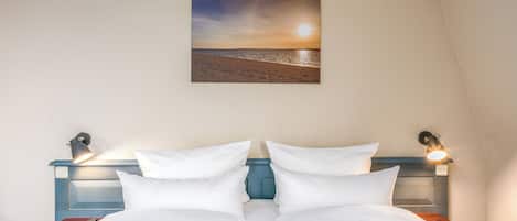 A bed with white bedding, a nightstand with a remote control, and a wall-mounted picture of a beach scene.