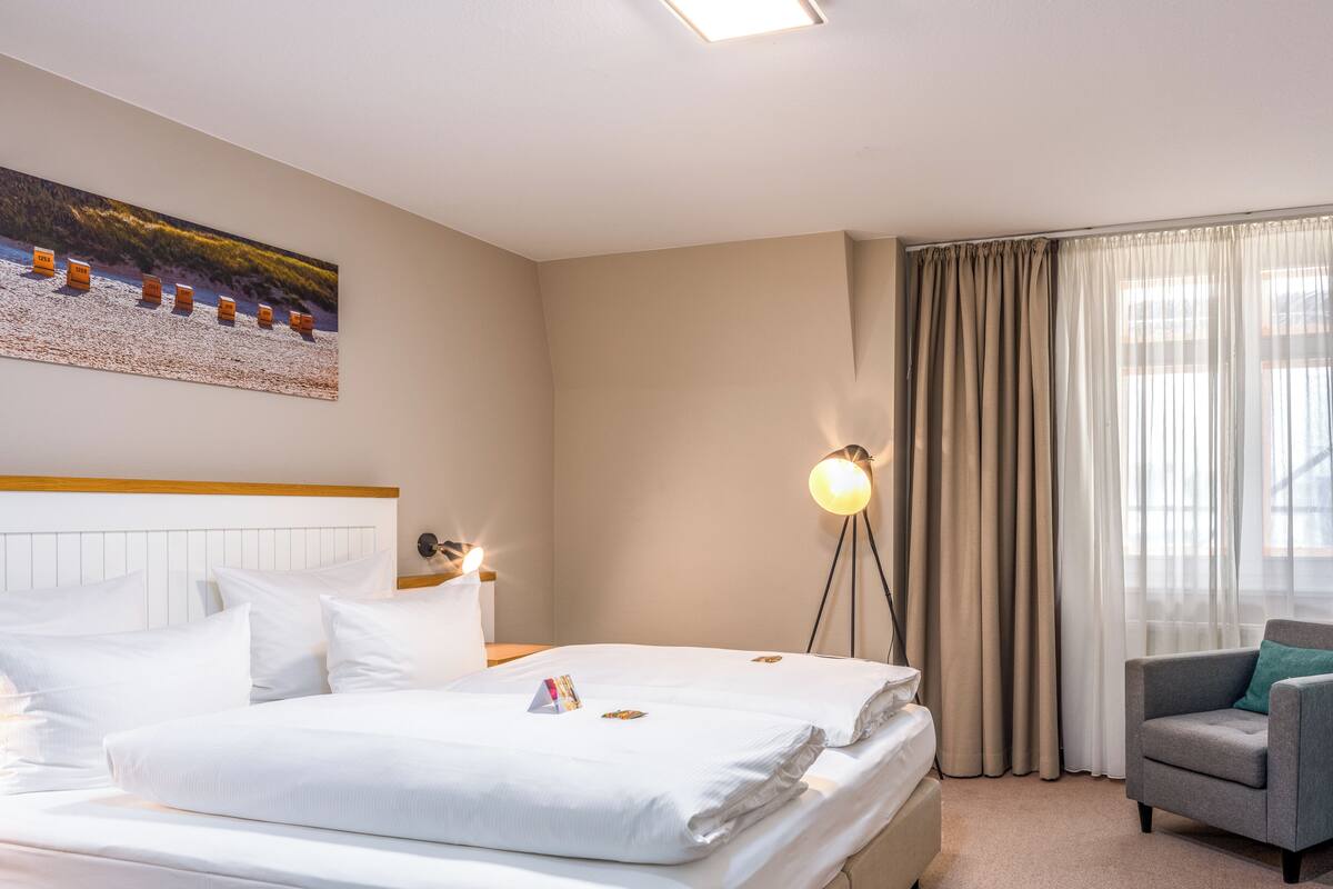 A hotel room with a bed, a chair, a lamp, and a painting on the wall.