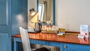 A hotel room with a wooden desk, a mirror, a kettle, and a tray with toiletries.