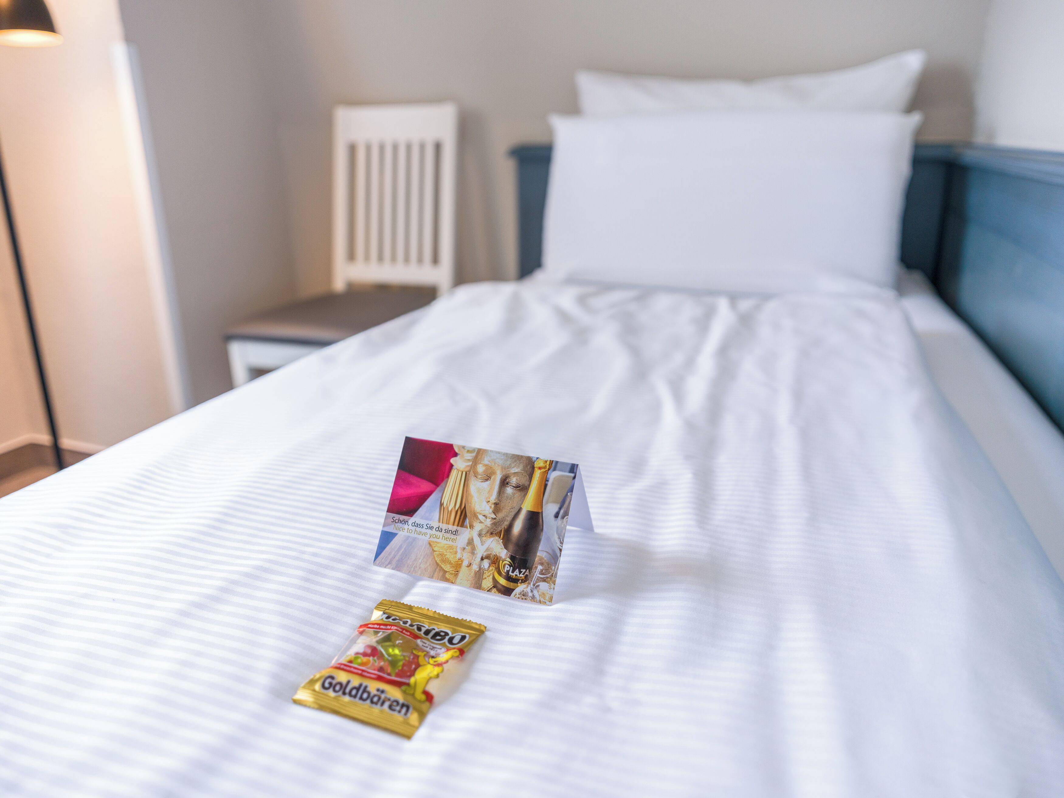 A neatly made bed with white linens, a small bedside table, and a lamp.