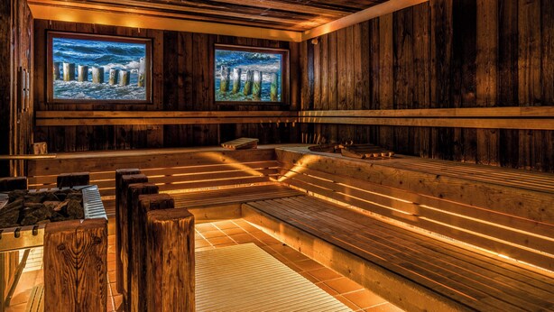 A sauna with wooden walls, benches, and two large windows with ocean scenes.