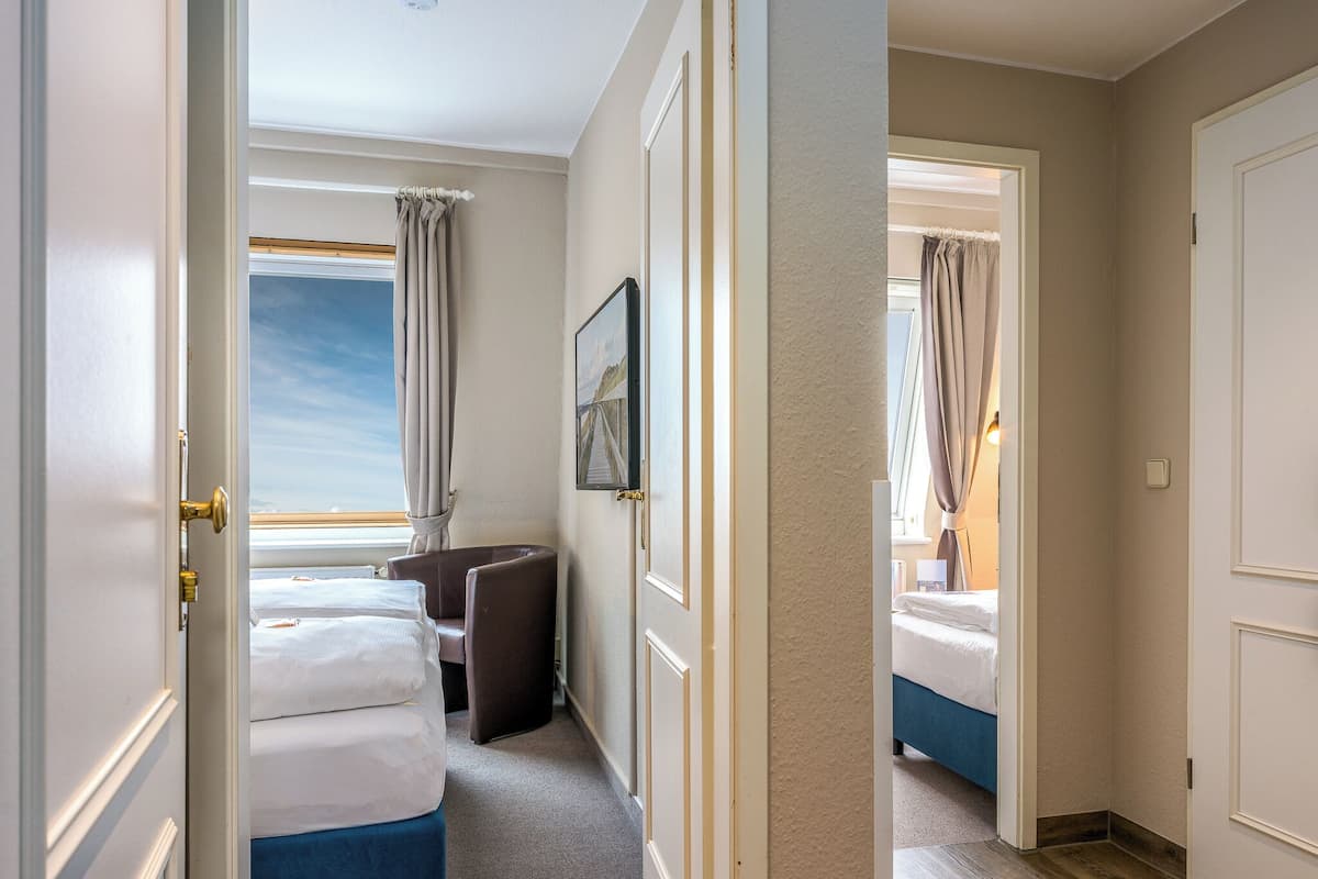 A hotel room with a bed, a chair, a desk, a window with curtains, and a framed picture on the wall.