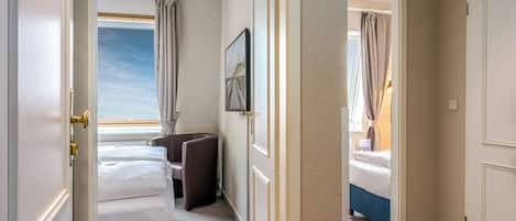 A hotel room with a bed, a chair, a desk, a window with curtains, and a framed picture on the wall.