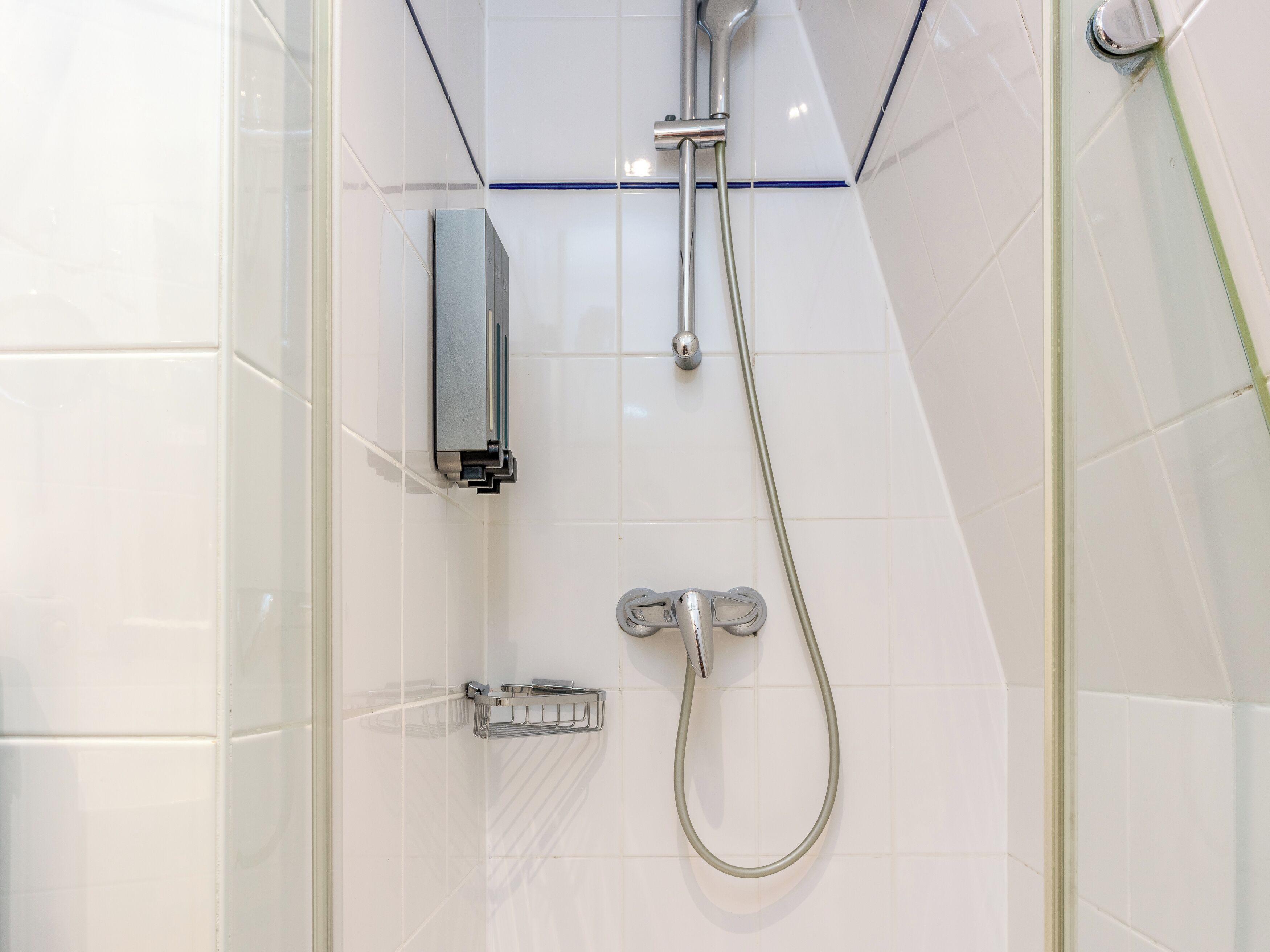 A shower with a handheld showerhead, a wall-mounted faucet, and a soap dish.