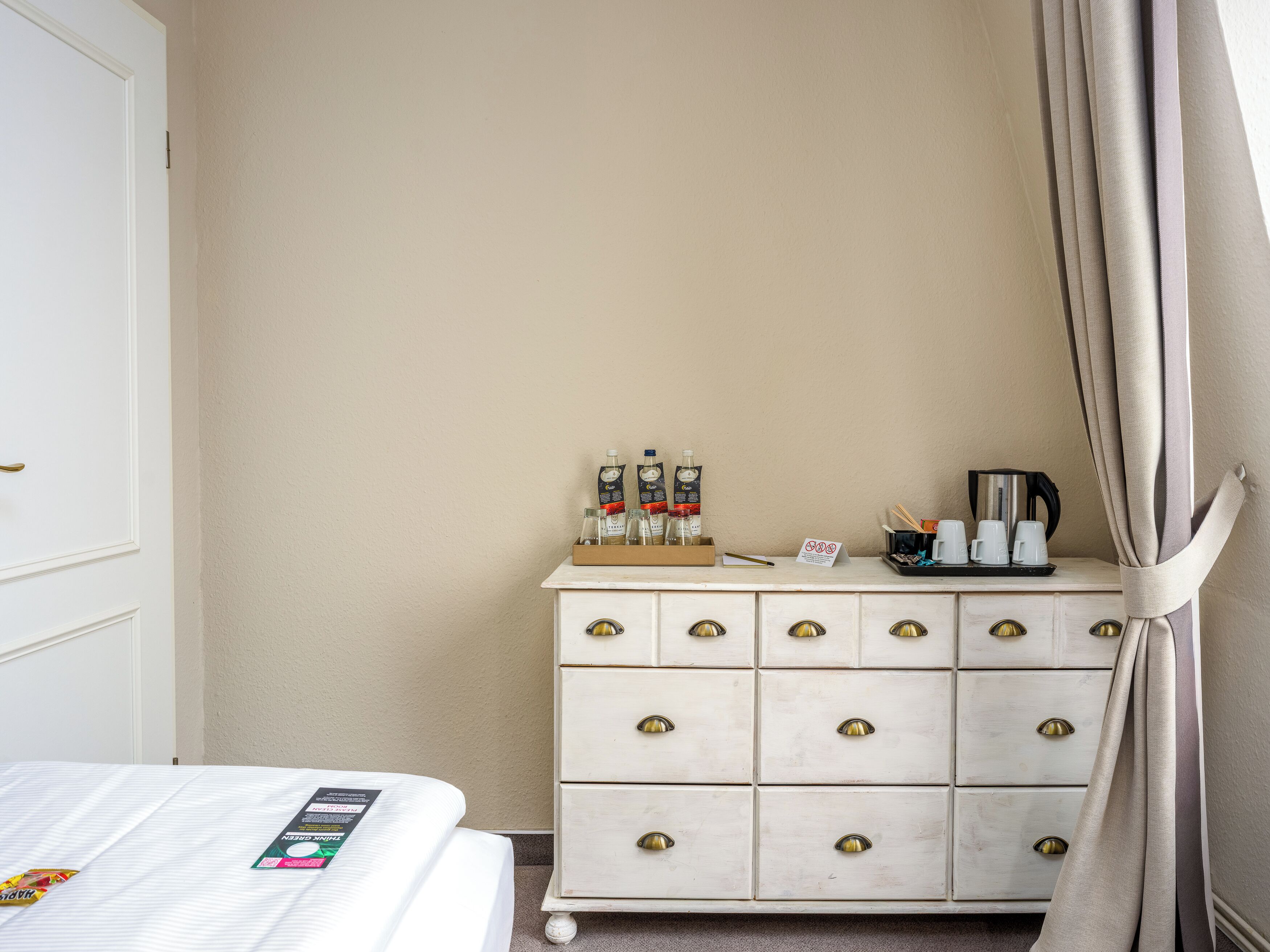 Una habitación de hotel con cama, cómoda con cajones, bandeja con artículos de aseo y cafetera.