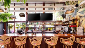 Eine Bar mit Korbstühlen, einem Fernsehbildschirm und einer Auswahl an Flaschen und Gläsern auf Regalen.