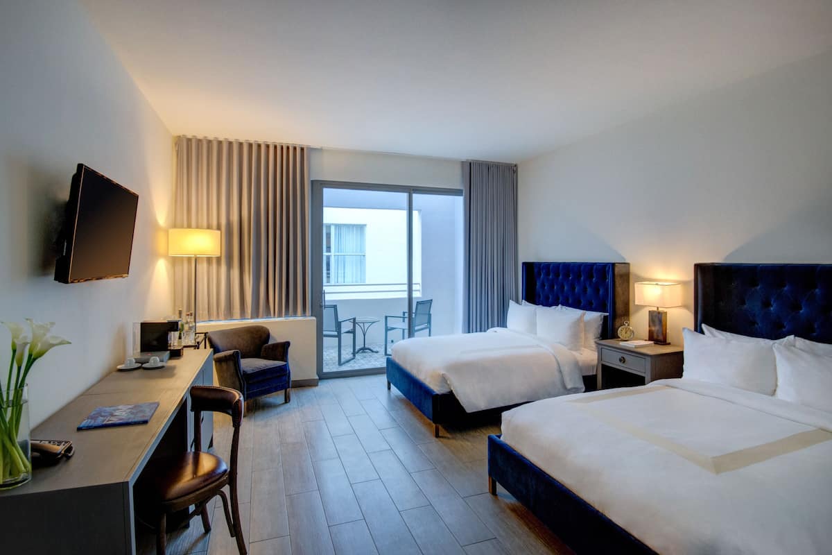 Habitación de hotel con dos camas, un escritorio, una silla, un televisor y un balcón con vistas.