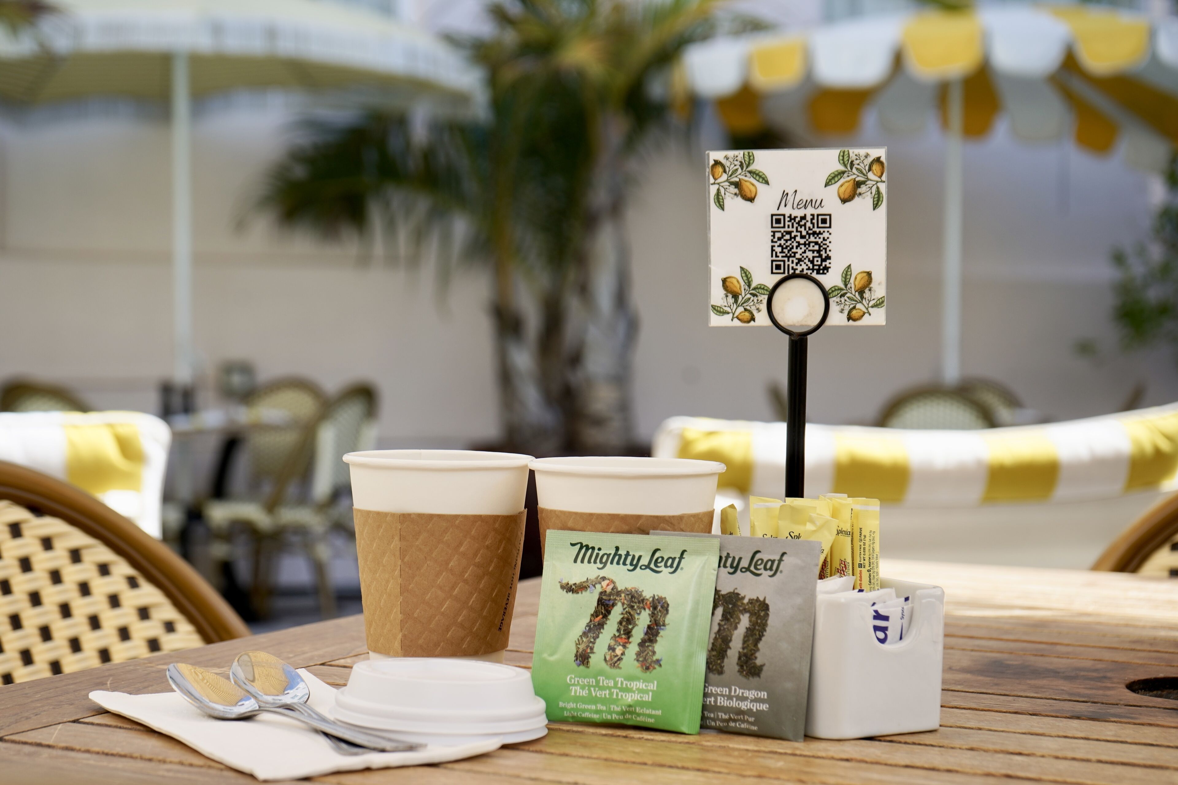 A table with a menu stand, two paper cups, tea bags, and a spoon.