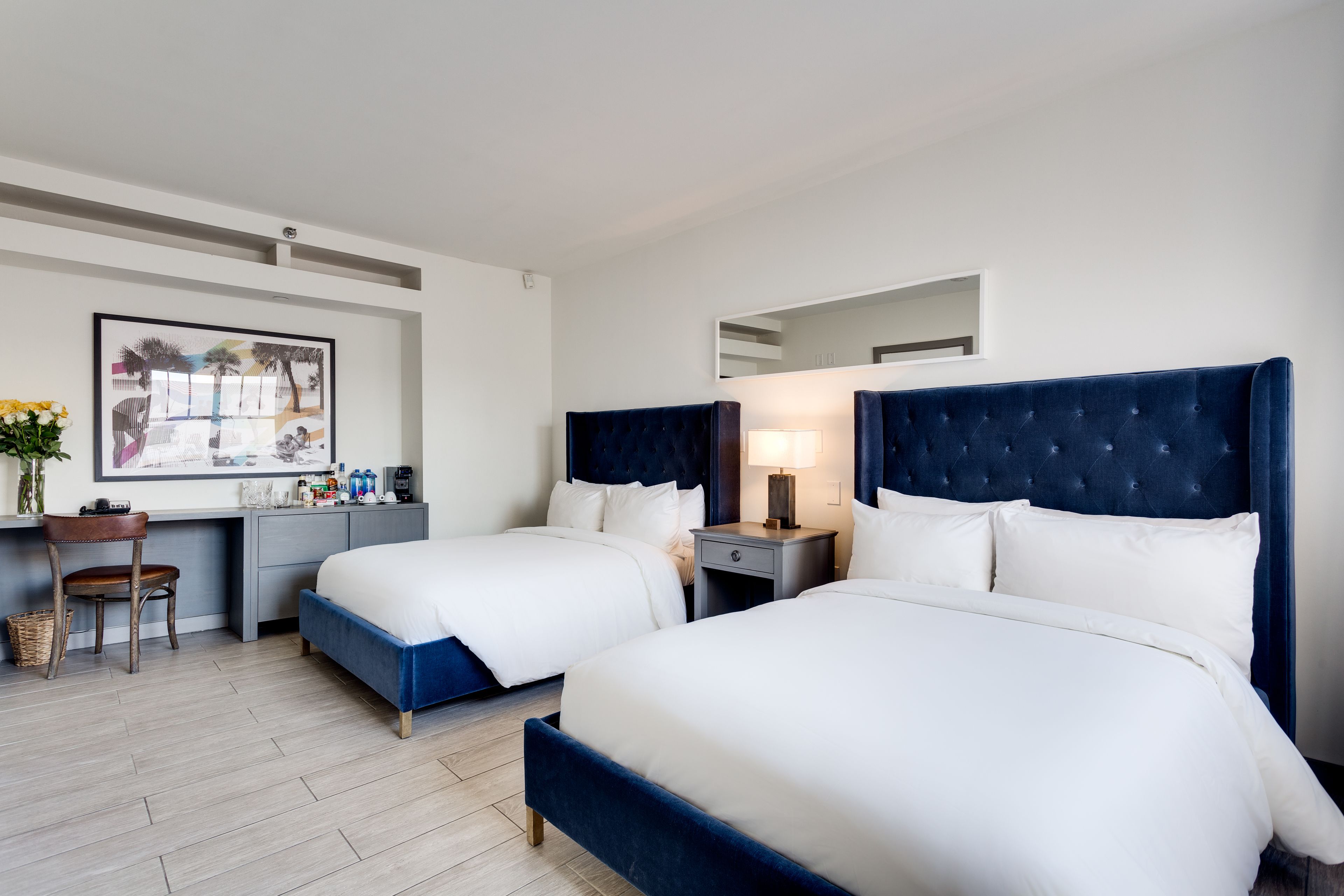 A hotel room with two beds, a desk, a chair, and a large framed picture on the wall.