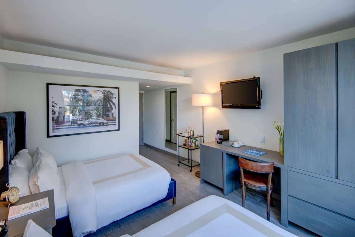 Una habitación de hotel con cama, escritorio, silla, televisor y un cuadro en la pared.