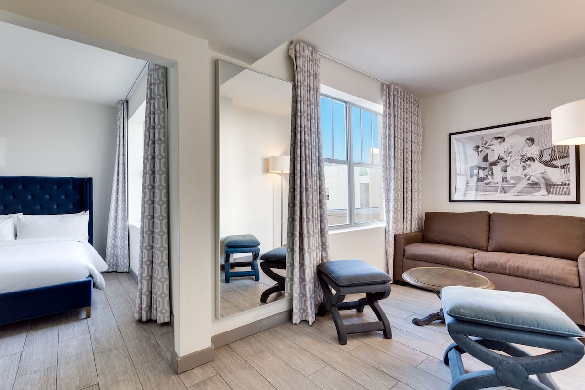 Una habitación de hotel con una cama, un sofá, una pequeña mesa y un espejo.
