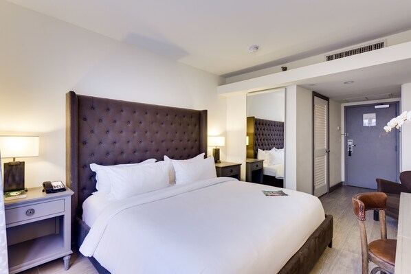 Une chambre d’hôtel avec un grand lit, une table de chevet avec un téléphone, une chaise et un bureau avec une lampe.