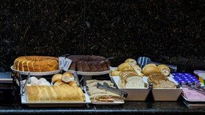 Un bufé con diversos alimentos, incluyendo pasteles, sándwiches y pan.