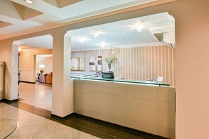 A hotel reception area with a glass partition, a reception desk, and a decorative plant. - Plaza Inn Executive - Setor Oeste (Goiania)