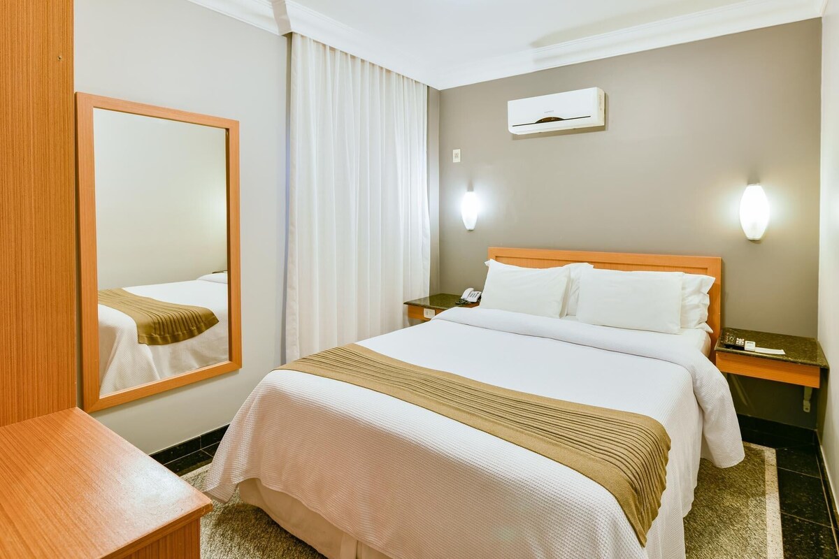 Habitación de hotel con cama, mesita de noche, espejo y aire acondicionado instalado en la pared.