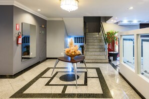 Un vestíbulo de hotel con una recepción, un extintor, una escalera y un ventanal grande.