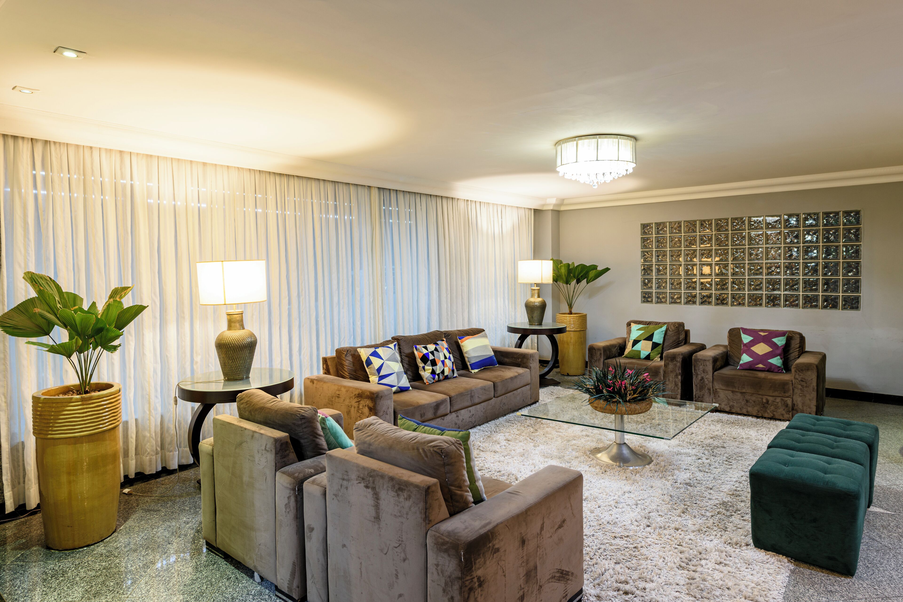 A spacious living room with a sofa set, two armchairs, a coffee table, and a large potted plant.