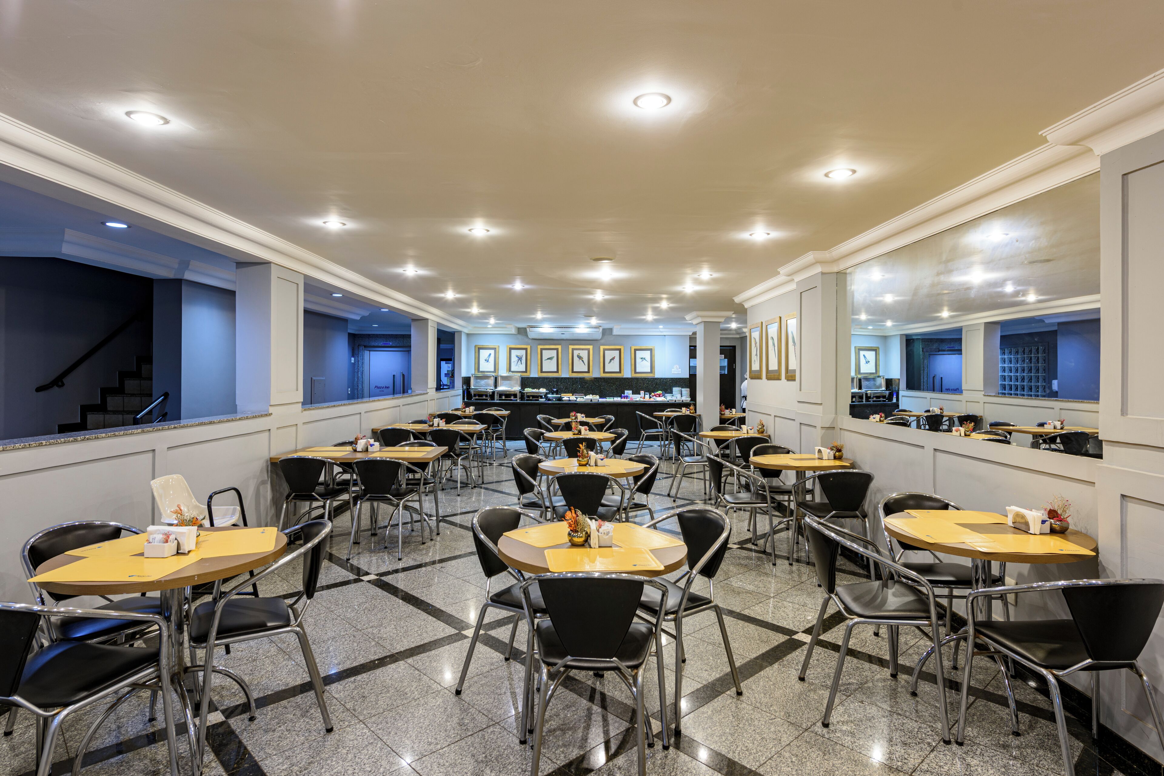 A spacious dining area with multiple tables and chairs, a counter with a cash register, and framed pictures on the walls.