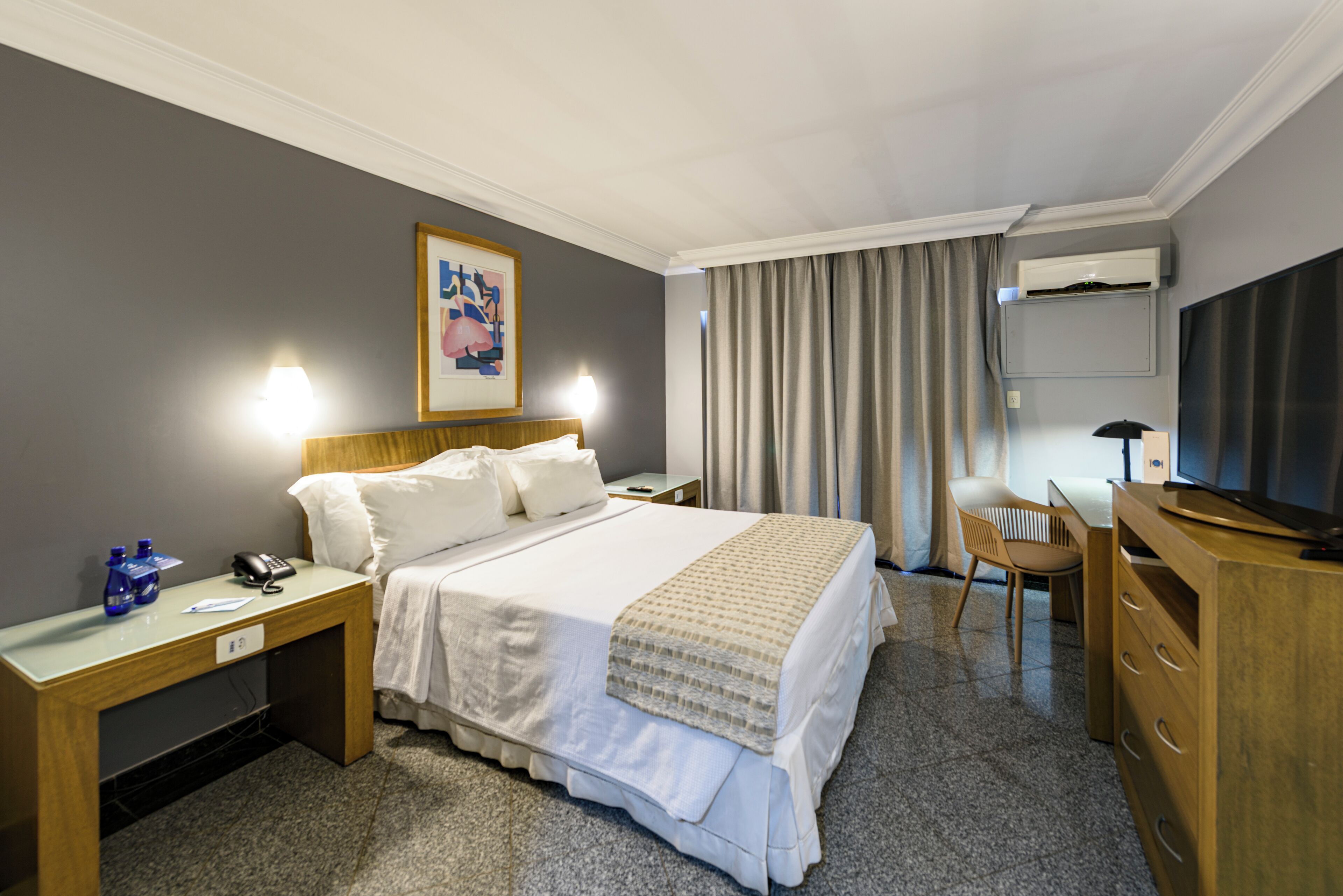 Una habitación de hotel con cama, mesita de noche, escritorio, silla y televisor.