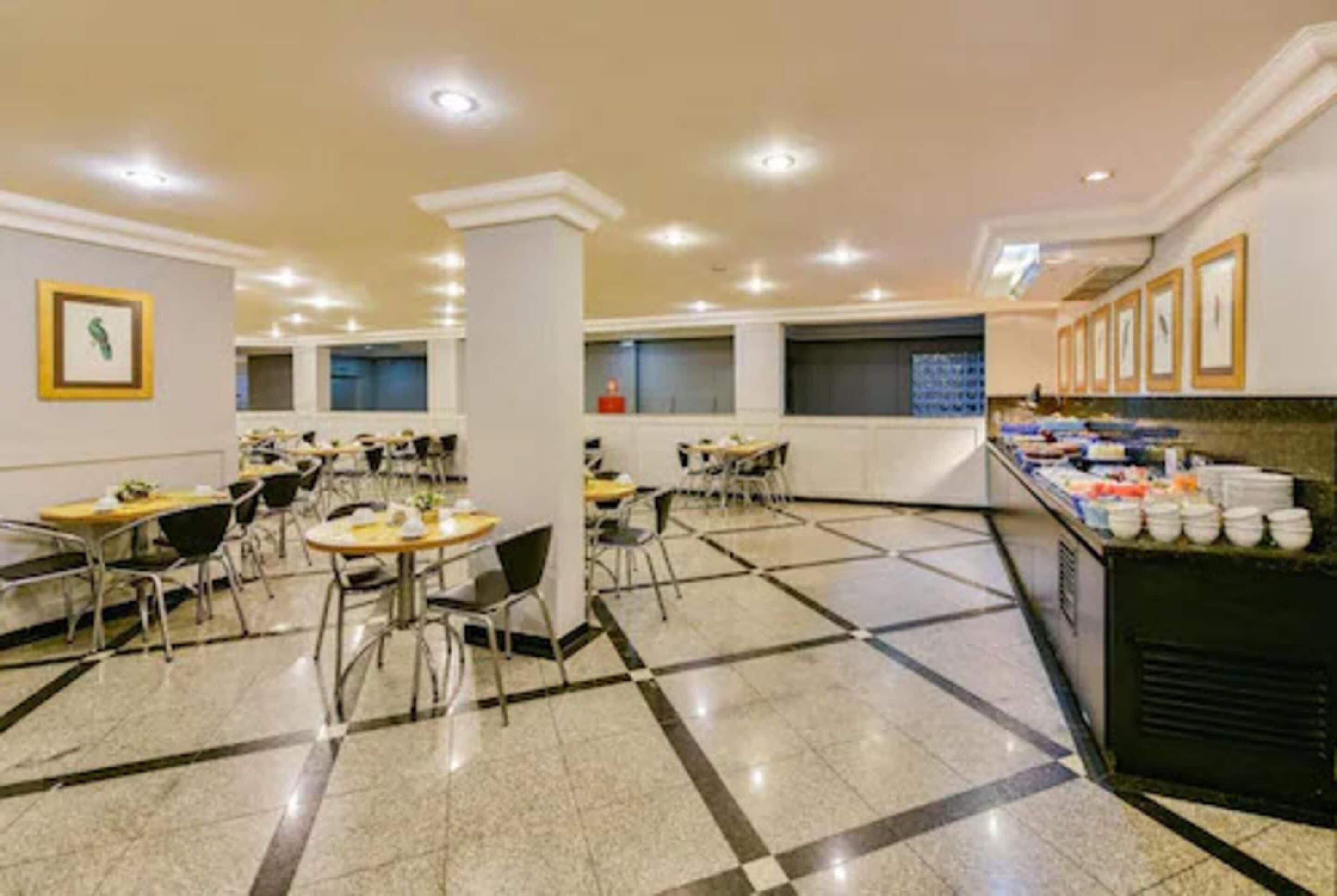 Un comedor amplio con varias mesas y sillas, una barra de buffet con diversas opciones de comida y un piso de baldosas.