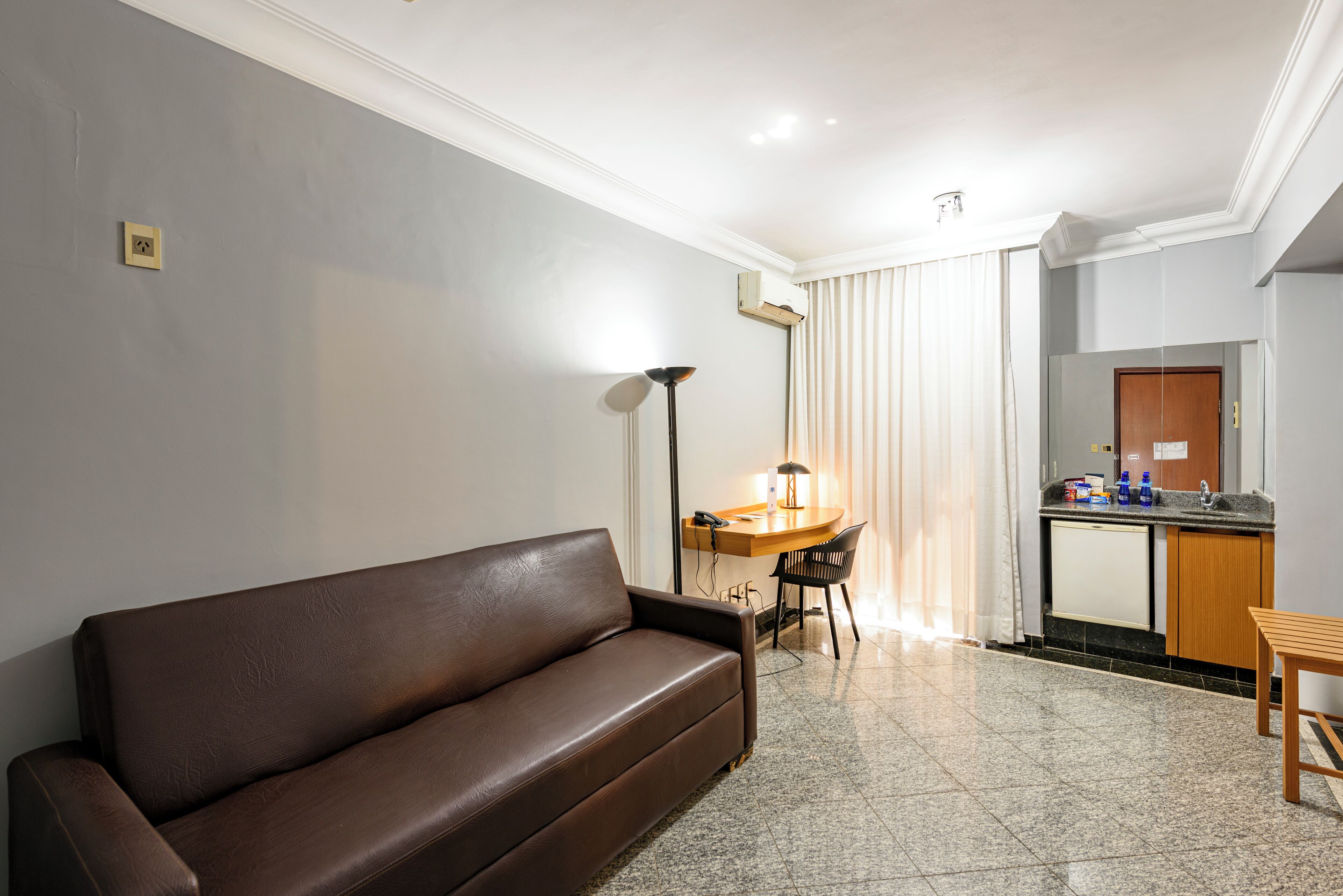 Una sala de estar moderna con un sofá de cuero marrón, una zona de comedor con una mesa y sillas de madera, y una cocina con un lavamanos y armarios.