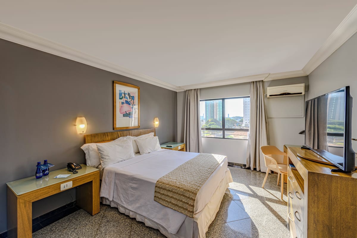 Ein Hotelzimmer mit Bett, Nachttischen, Schreibtisch mit Stuhl, Fernseher und einem Fenster mit Vorhängen.