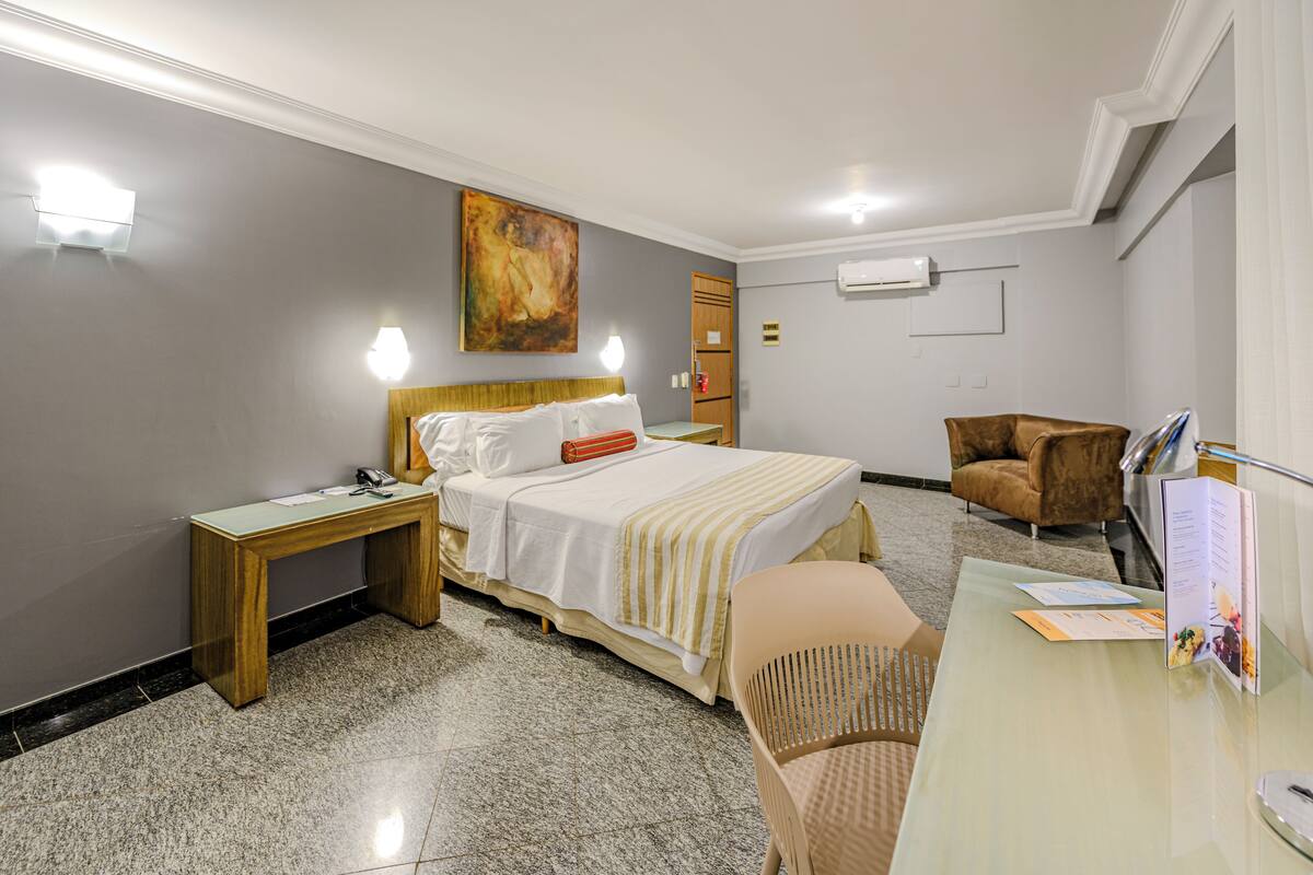 Ein Hotelzimmer mit Bett, Nachttisch, Stuhl, Schreibtisch und einem Bild an der Wand.