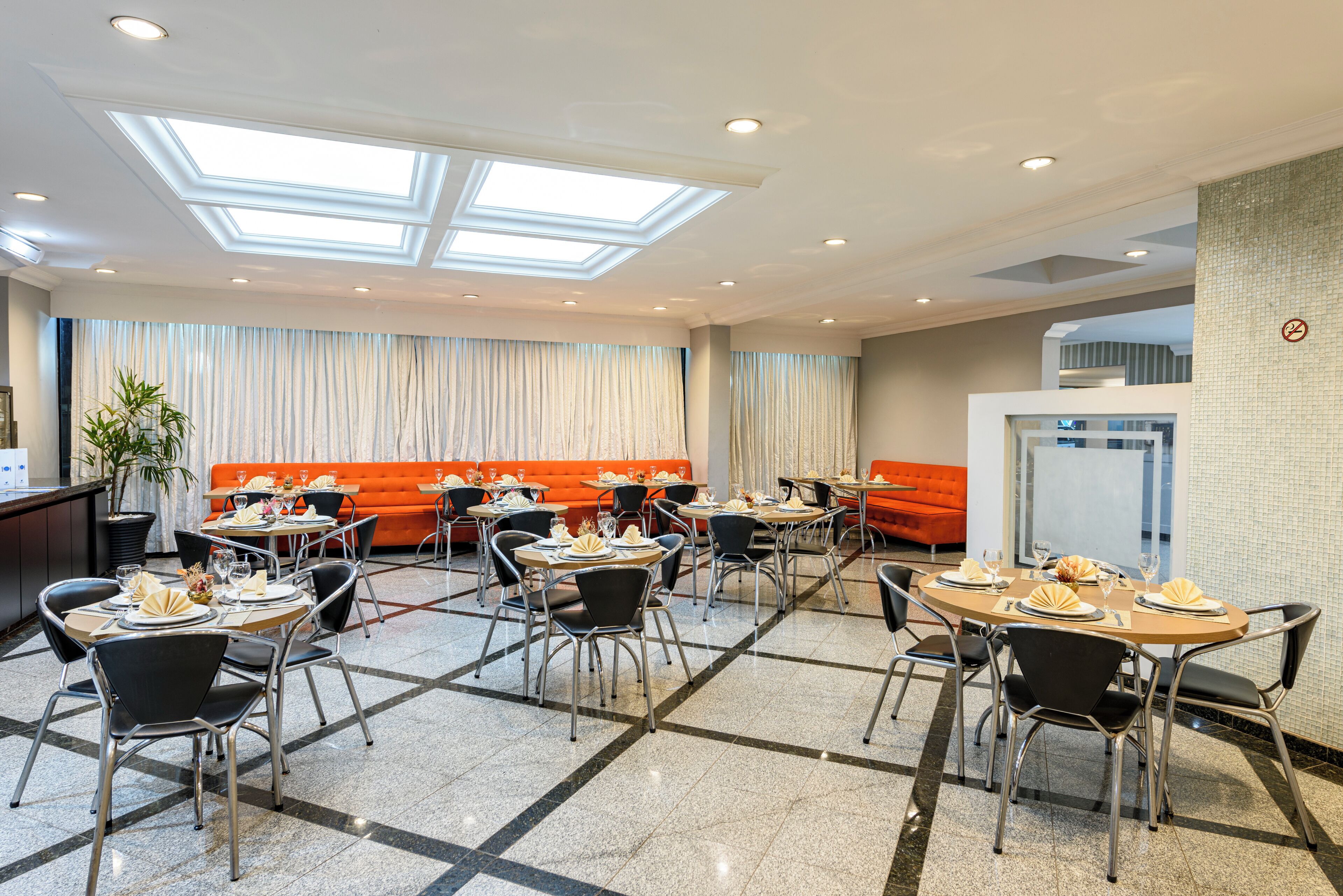 A hotel dining area with multiple tables and chairs, a sofa, and a potted plant.
