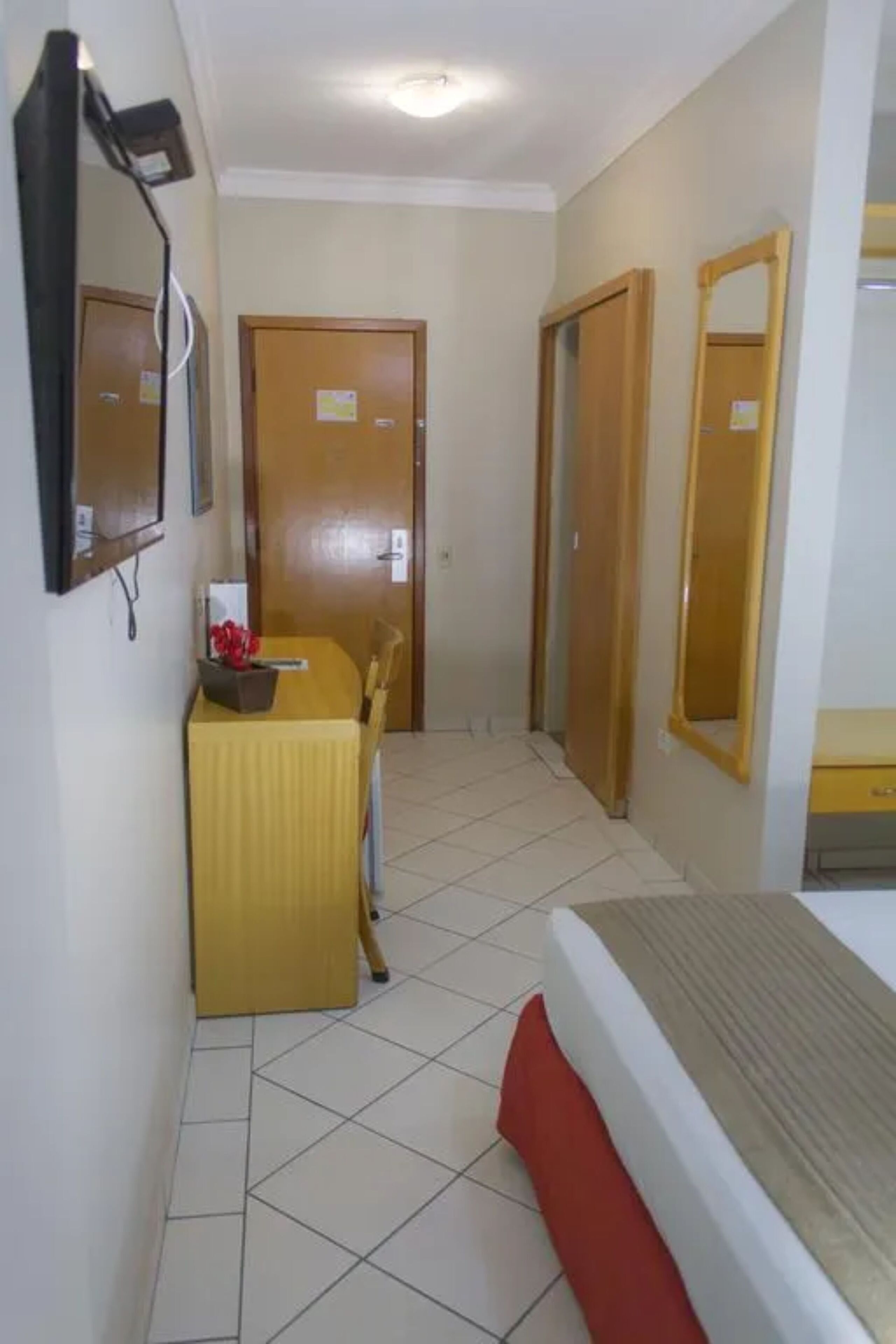 A hotel room with a bed, a desk with a chair, a mirror, and a door.