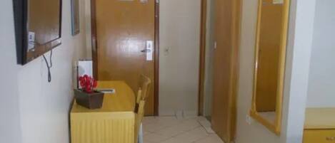 A hotel room with a bed, a desk with a chair, a mirror, and a door.
