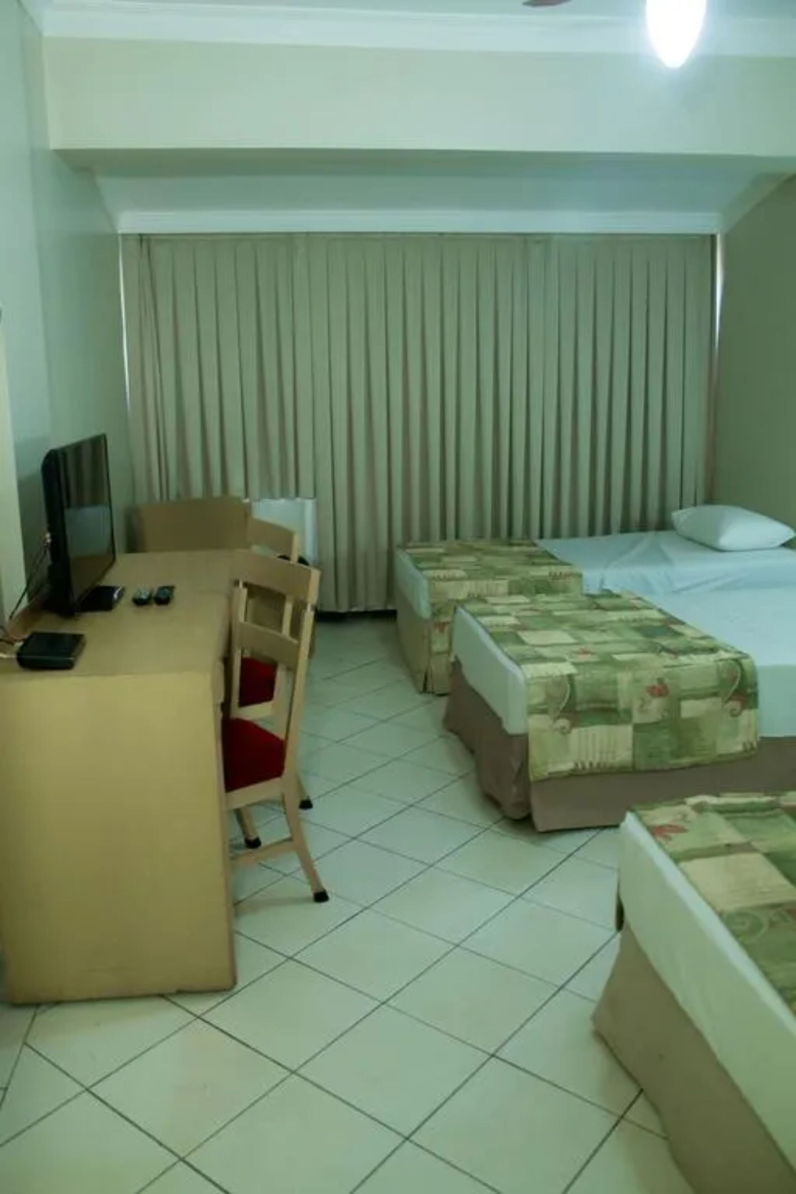 Una habitación de hotel con escritorio, dos camas, una silla, televisor y cortinas.