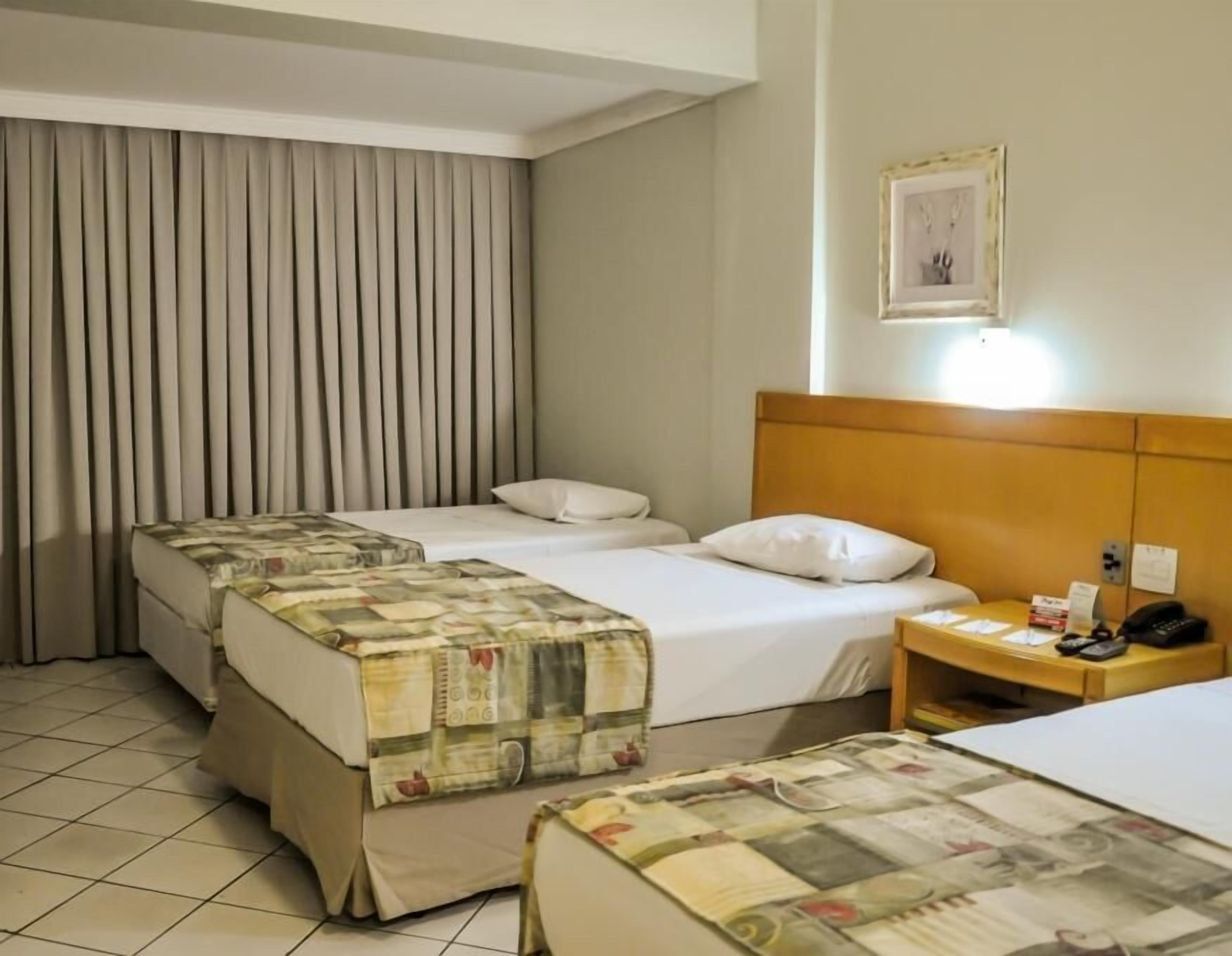 A hotel room with two beds, a nightstand, a framed picture, and a curtain.