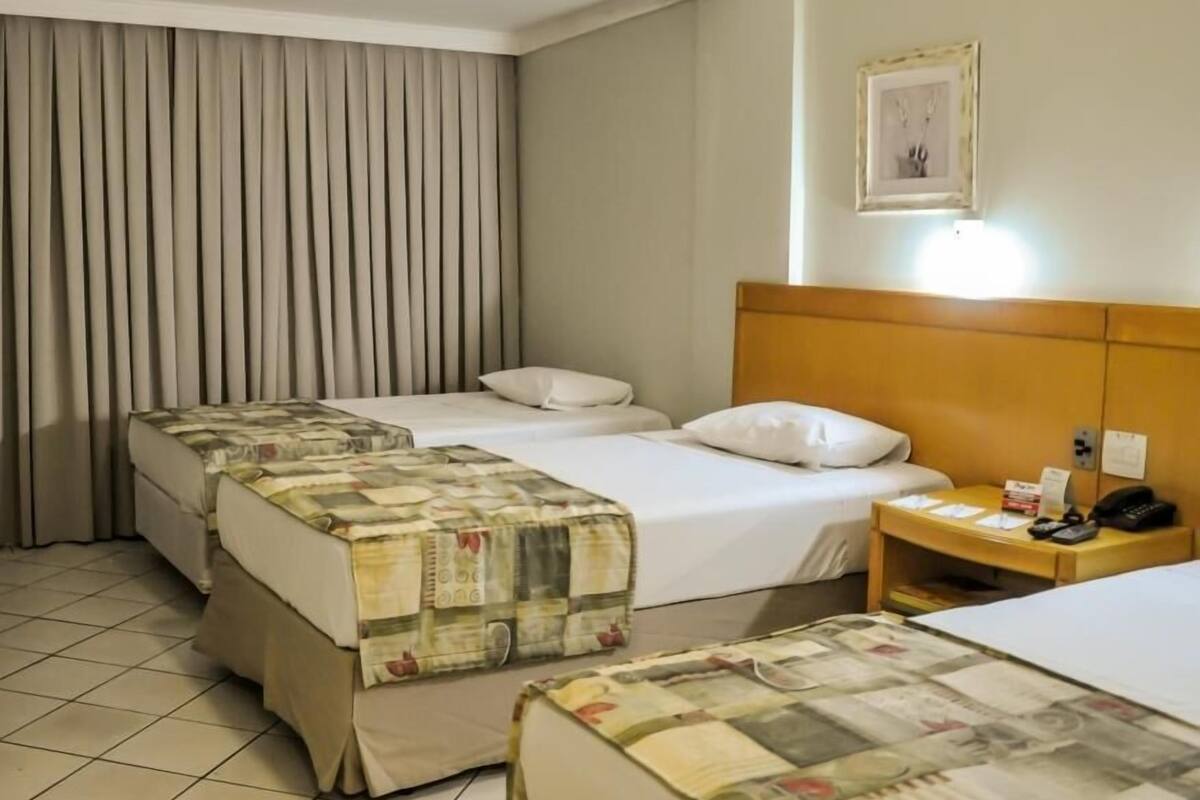 A hotel room with two beds, a nightstand, a framed picture, and a curtain.